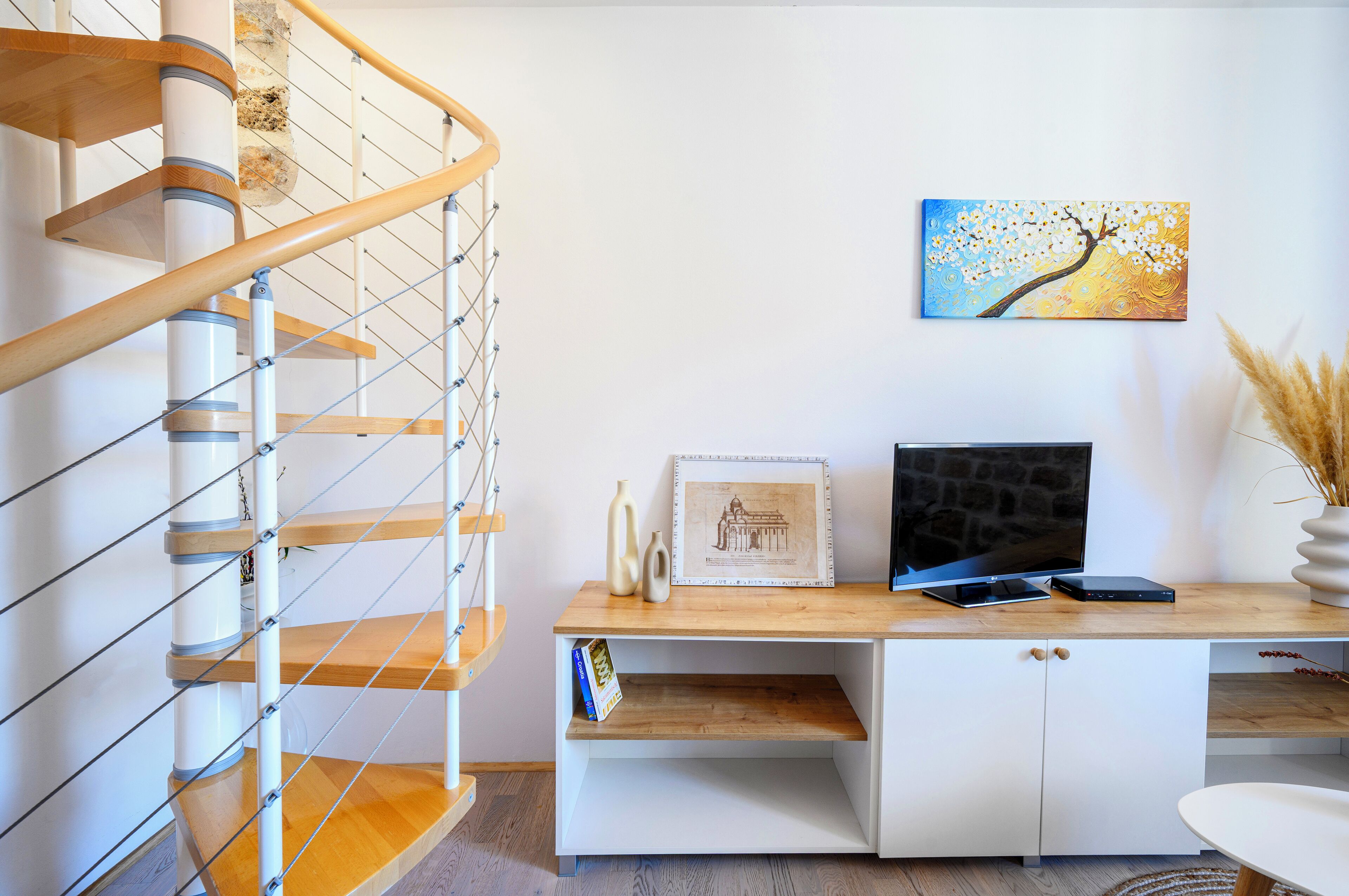 A staircase with wooden railings and a white wall with a framed picture and a flat-screen TV on a wooden desk.
