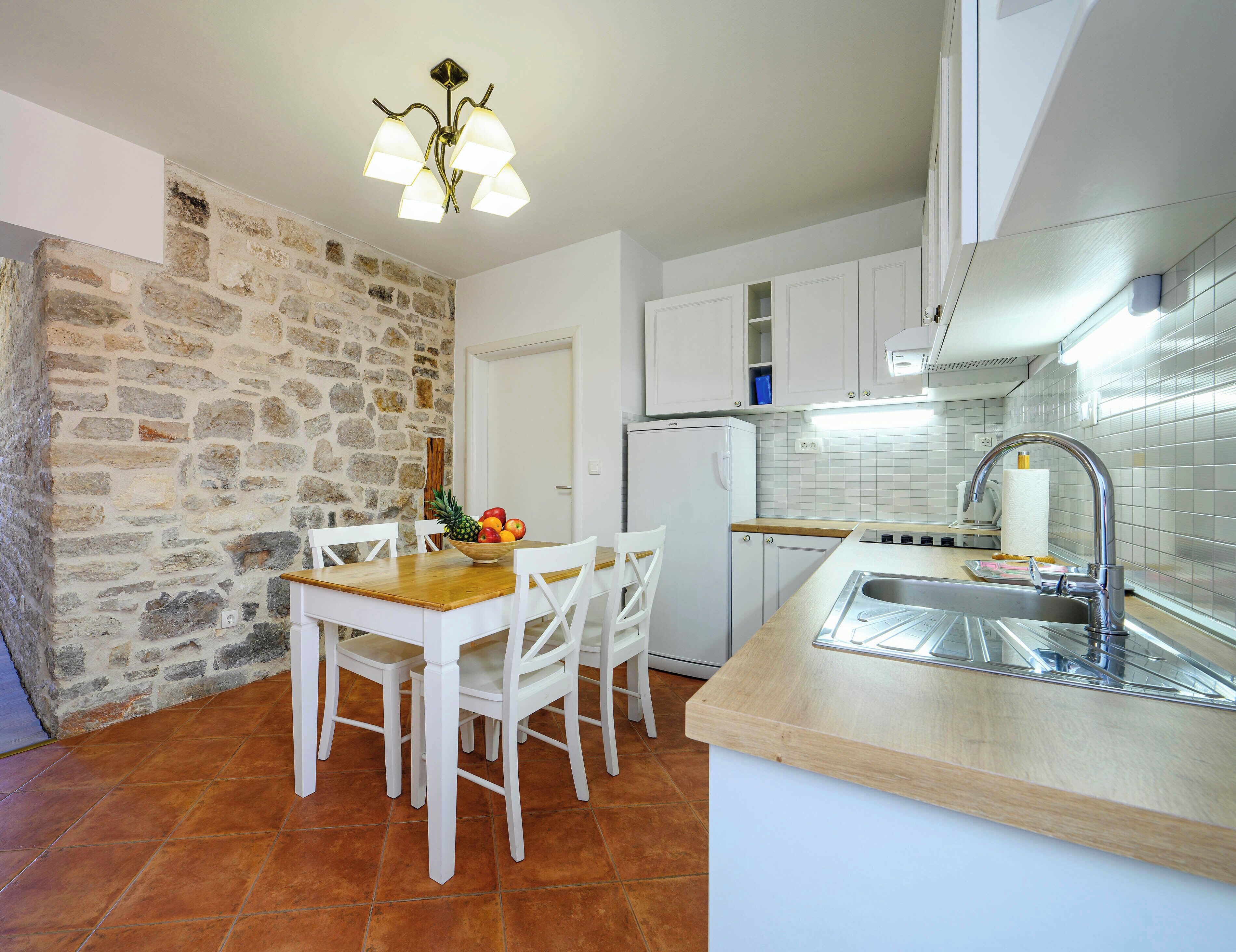 A kitchen with white cabinets, a wooden table, and a stone wall.