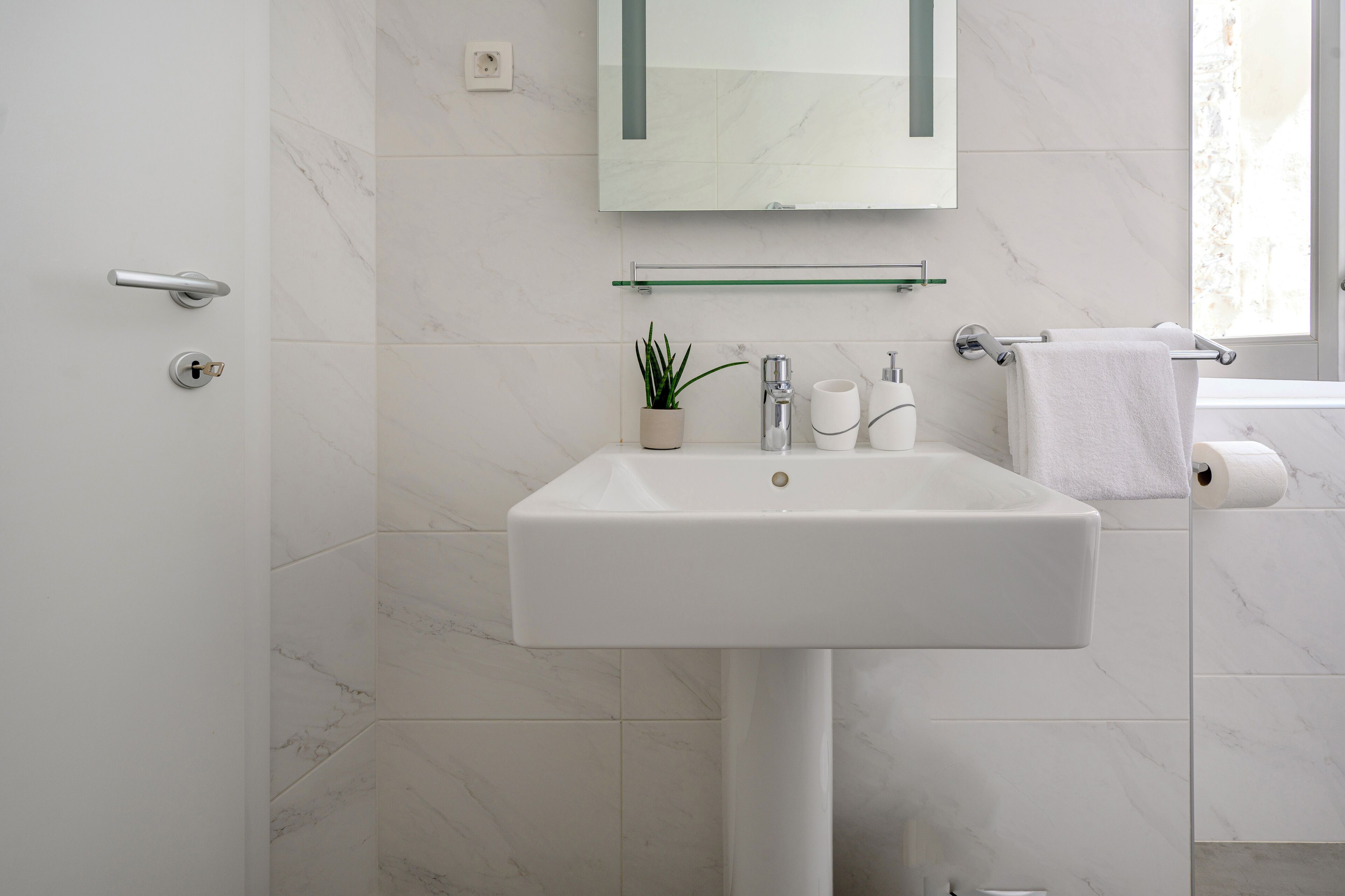 A bathroom with a white sink, a mirror, a towel rack, and a potted plant.
