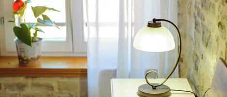 A room with a bed, a bedside table with a lamp, a potted plant, and a window with curtains.