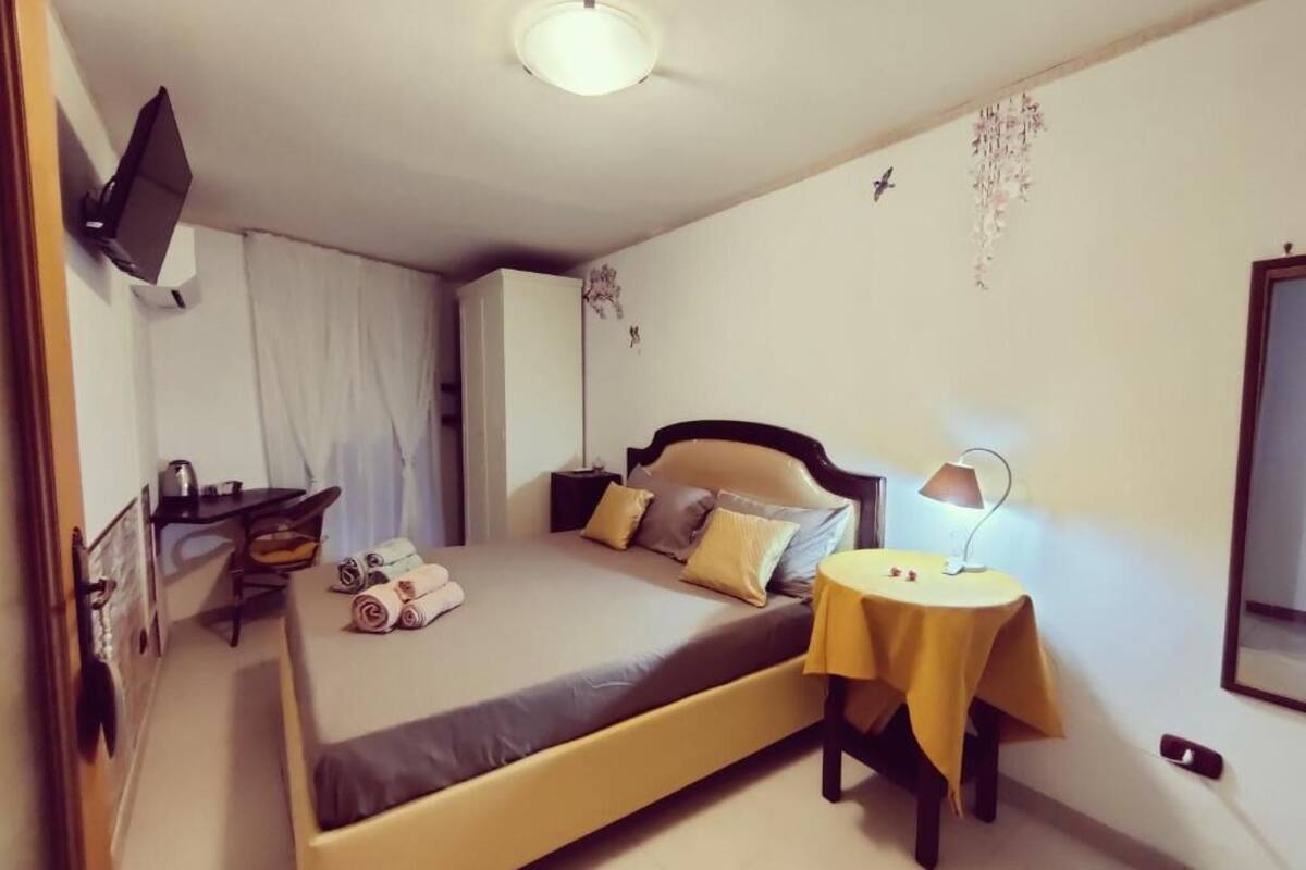 A bedroom with a bed, bedside table, lamp, and a TV mounted on the wall.