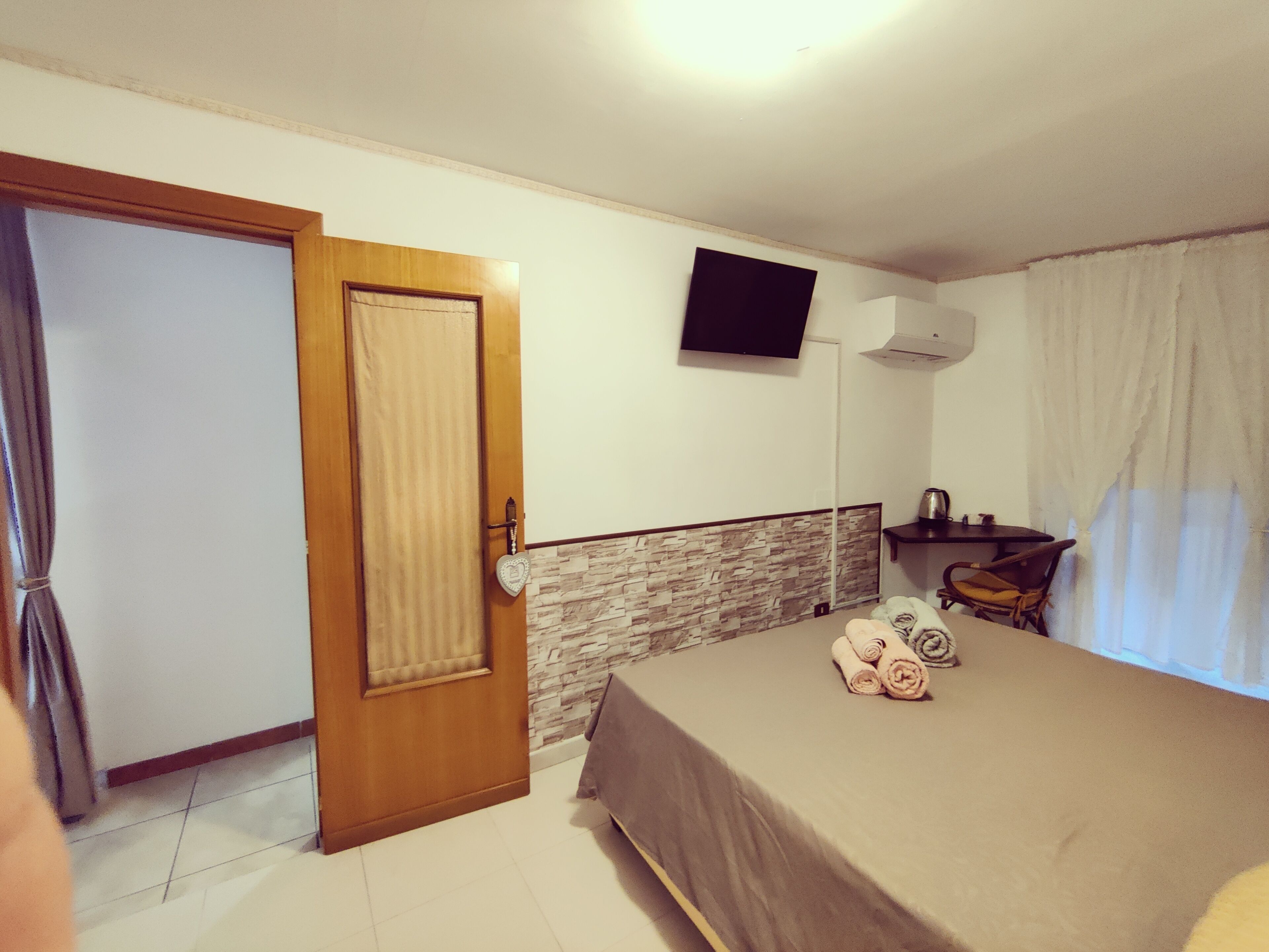 Ein Hotelzimmer mit Bett, Fernseher an der Wand, Schreibtisch mit Stuhl und einem Vorhangfenster.