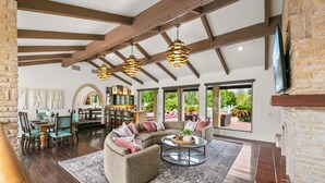 A spacious living area with a sectional sofa, a round coffee table, and a dining table with chairs. There are large windows offering views of the outdoors. - 20 Beds, 2 Pickleball Courts, Basketball, 4 Acres,
Gym and Gameroom (Bermuda Dunes)