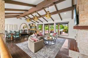 A spacious living area with a sectional sofa, a round coffee table, and a dining table with chairs. There are large windows offering views of the outdoors. - 20 Beds, 2 Pickleball Courts, Basketball, 4 Acres,
Gym and Gameroom (Bermuda Dunes)
