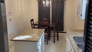 A kitchen with a central island, a dining table with chairs, a chandelier, and a ceiling fan.