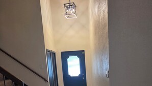 A hallway with a staircase, a door with a window, and a hanging light fixture.