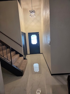 A hallway with a staircase, a door with a window, and a hanging light fixture. - <8mi FIFAWorldCup Arlington CowBoysATT GlobeLife TexasRangers SixFlags Free Park (Arlington)