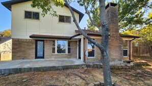 A two-story house with a brick exterior, a front porch, and a tree in the yard.
