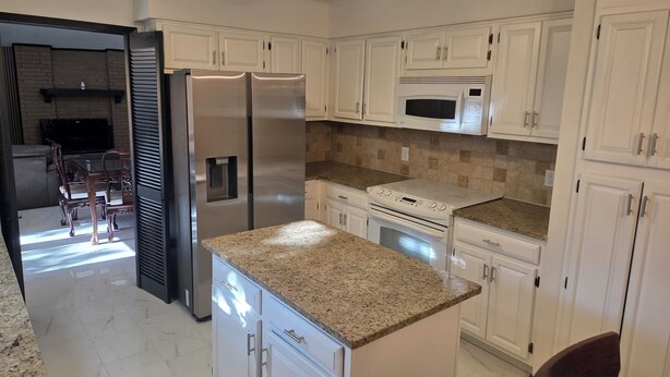 A kitchen with white cabinets, stainless steel appliances, granite countertops, and a ceiling fan.