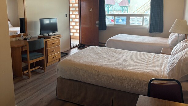 A hotel room with two beds, a desk with a computer, a TV, and a window with a view of the outside. - Casey's Inn (Lac du Bonnet)