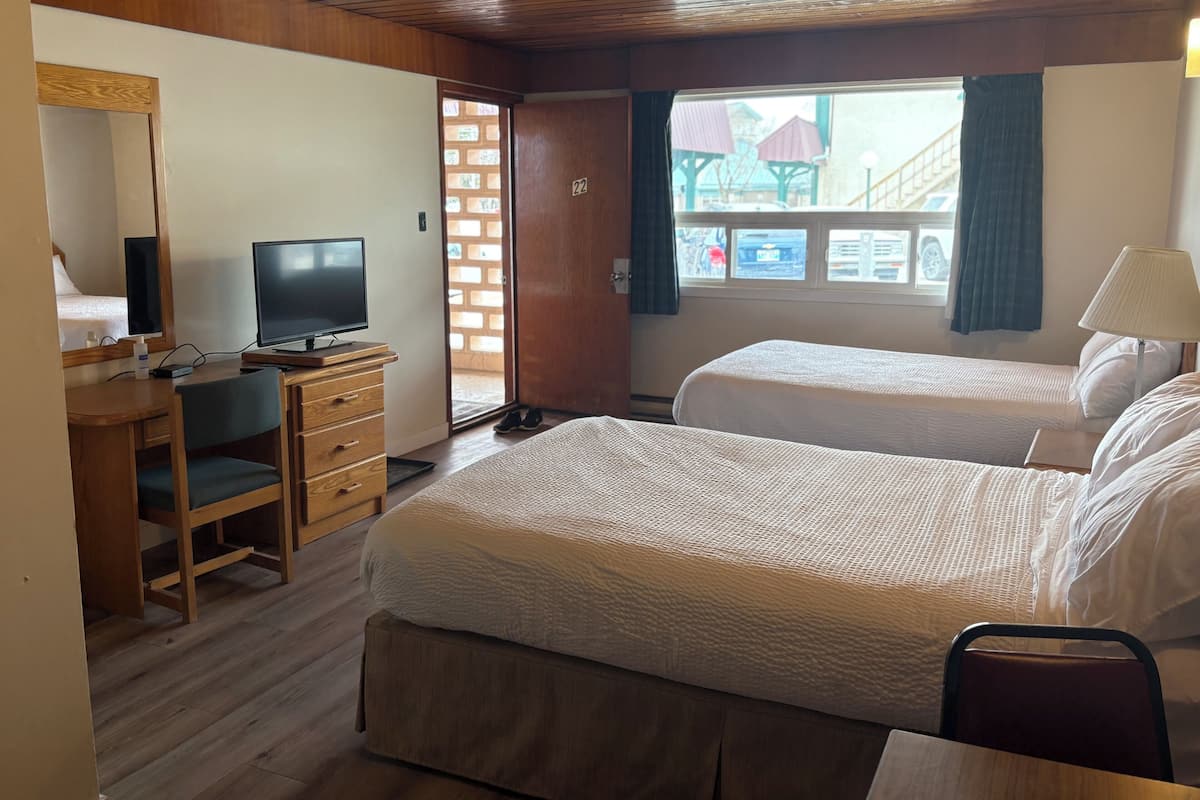 Habitación de hotel con dos camas, un escritorio con una computadora, un televisor y una ventana con vista al exterior.
