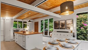 A modern kitchen with white cabinetry, a wooden ceiling, and a dining area with a white table set for four. - Burke Bay A-Frame Retreat w/Cedar Hot Tub - 15 Minutes to Seattle Ferry (Bremerton)