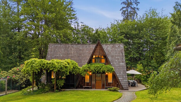 A wooden cabin with a sloped roof, surrounded by lush greenery and a paved pathway leading to the entrance. - Burke Bay A-Frame Retreat w/Cedar Hot Tub - 15 Minutes to Seattle Ferry (Bremerton)