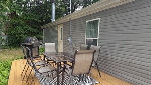 A deck with a table and chairs, a grill, and a window.