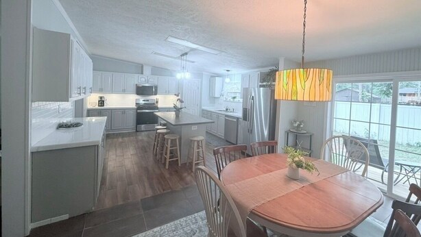 A modern kitchen with white cabinets, a dining area with a wooden table, and a large window with a view.