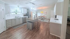 A modern kitchen with white cabinetry, a central island, and a dining area with a table and chairs.