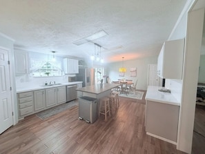 A modern kitchen with white cabinetry, a central island, and a dining area with a table and chairs. - Delightful 4-bedroom house across from Warren Dunes! (Sawyer)