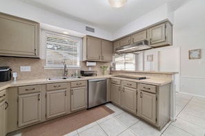A kitchen with beige cabinets, a dishwasher, a sink, and a window with blinds.