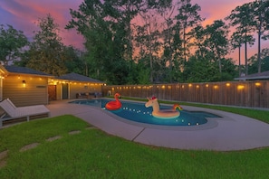 A backyard with a swimming pool, a wooden deck, a lounge chair, and a fence.