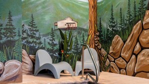 Un'area benessere con parete in pietra, un murale raffigurante una piccola casetta di legno e una piscina.