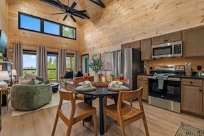 A wooden interior with a dining table, chairs, a sofa, and a kitchen area including a refrigerator and microwave. - Indoor Pool, Mtn Views, Hot Tub, Couples Cabin, Fire Pit, & Close to Strip (Pigeon Forge)