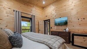 Una stanza con pannelli in legno, un letto, una cassettiera, una TV e una finestra con tende.