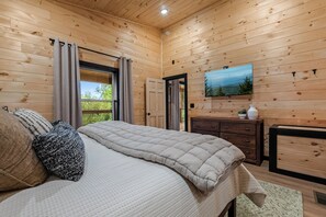 A wooden-paneled room with a bed, a dresser, a TV, and a window with curtains. - Indoor Pool, Mtn Views, Hot Tub, Couples Cabin, Fire Pit, & Close to Strip (Pigeon Forge)