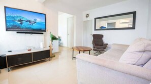 A modern living room with a flat-screen TV, a sofa, a chair, and a small table. - 2Bedroom Apt. With Small Swimming Pool (San Juan)