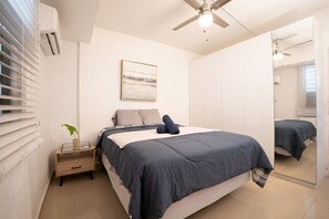 Ein Schlafzimmer mit einem Bett, einem Nachttisch, einem Spiegel und einem Deckenventilator.