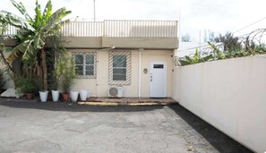 A building with a flat roof, a white door, and a small air conditioning unit. There are potted plants and a banana tree in front. - 2Bedroom Apt. With Small Swimming Pool (San Juan)