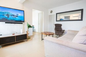 Ein modernes Wohnzimmer mit Flachbildfernseher, einer Couch, einem Sessel, einem kleinen runden Tisch und einem Topf mit Pflanze.