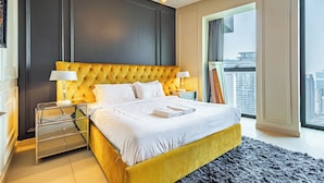Quarto de hotel moderno com uma cama grande, duas mesas de cabeceira, um candelabro e vista para a cidade.