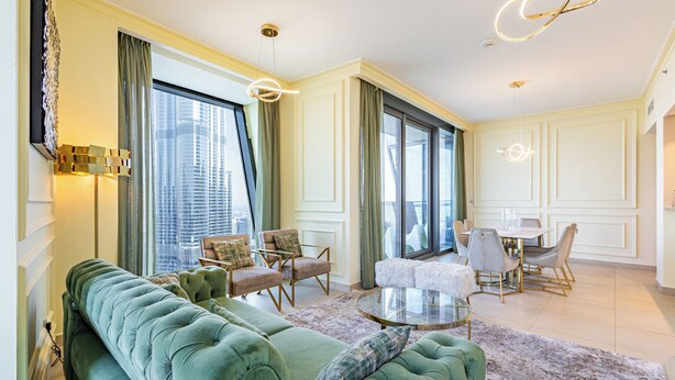 Uma sala de estar espaçosa com um sofá verde, uma mesa de centro redonda e uma área de jantar com mesa e cadeiras brancas.