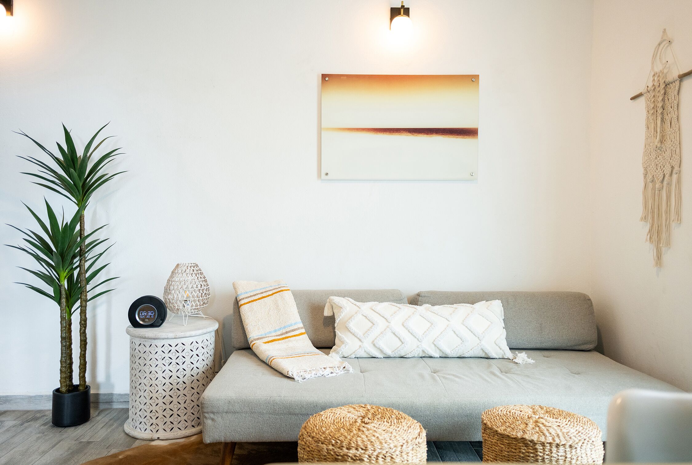 Un salon moderne avec un canapé gris, deux plantes en pot, une œuvre d’art accrochée au mur et une décoration murale en macramé.