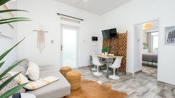 A modern living room with a sofa, a dining table with chairs, a television, and a wooden partition.