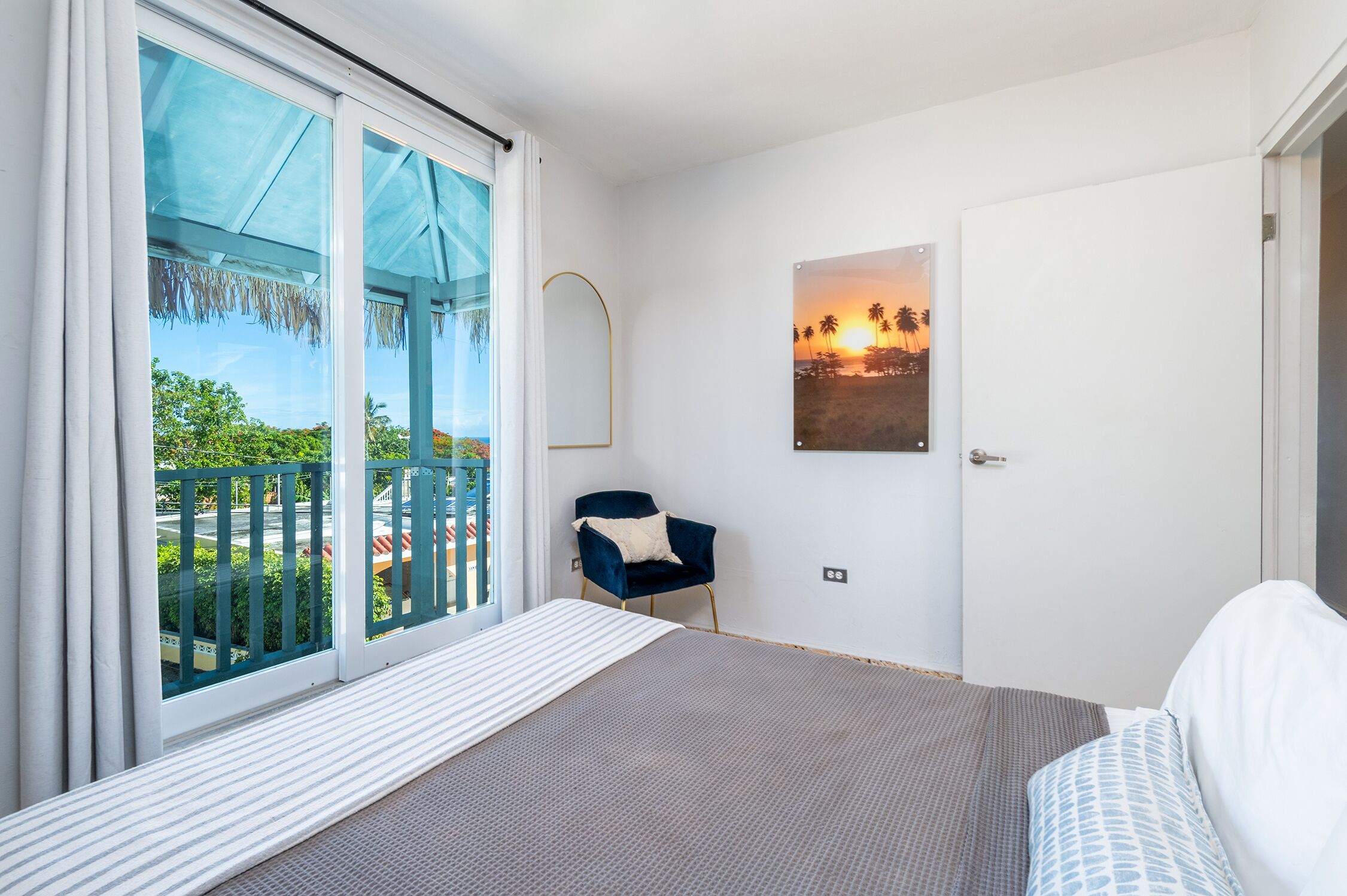 A bedroom with a bed, a chair, a window with a view, and a door.