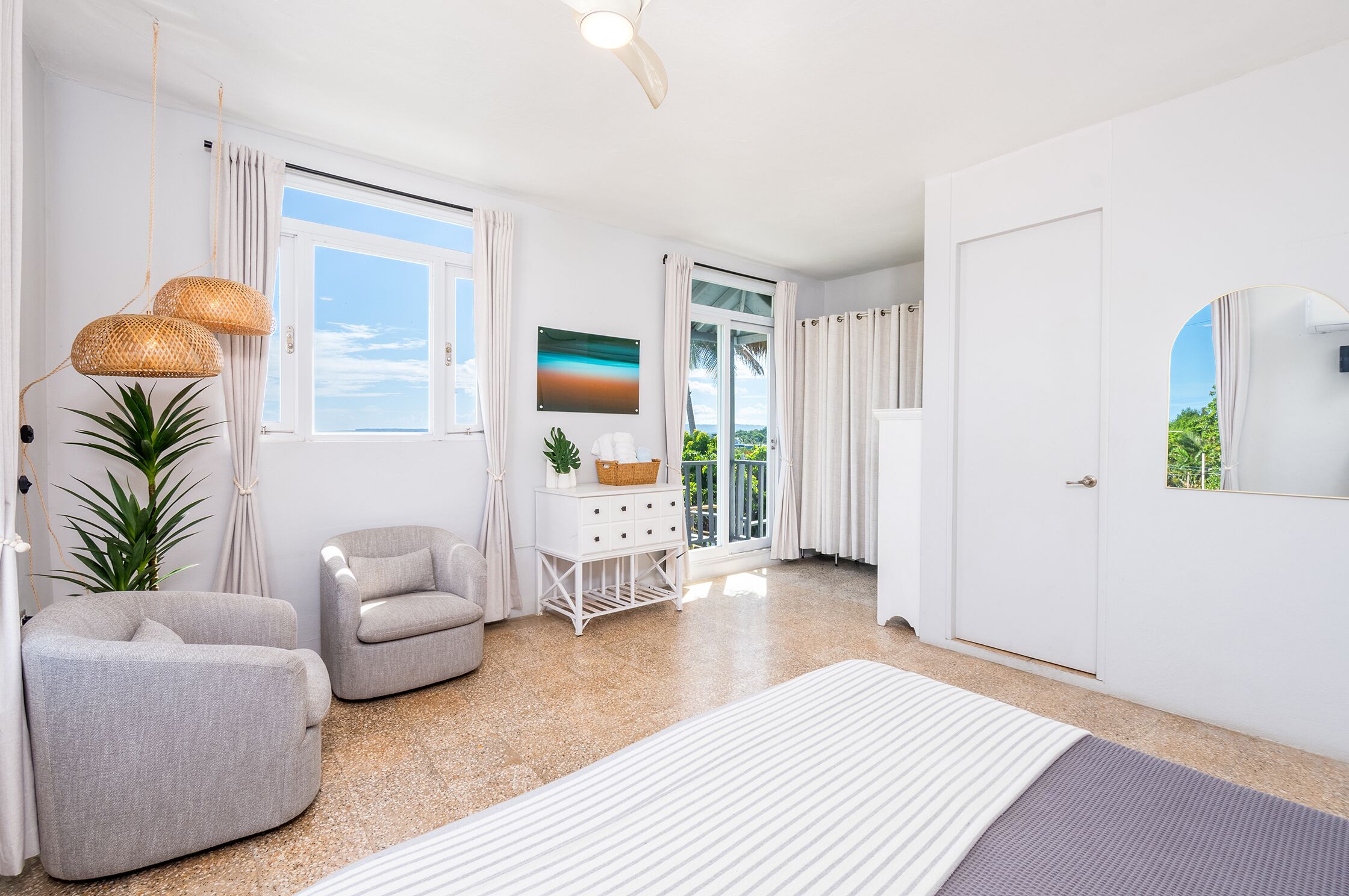 Une chambre d’hôtel moderne avec une grande fenêtre, une porte blanche, un canapé, une petite table et une plante.