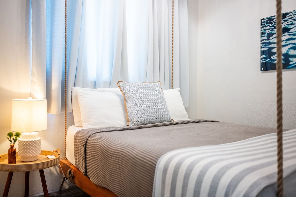 A bed with a striped blanket, a pillow with a geometric pattern, and a bedside table with a lamp and a small vase.