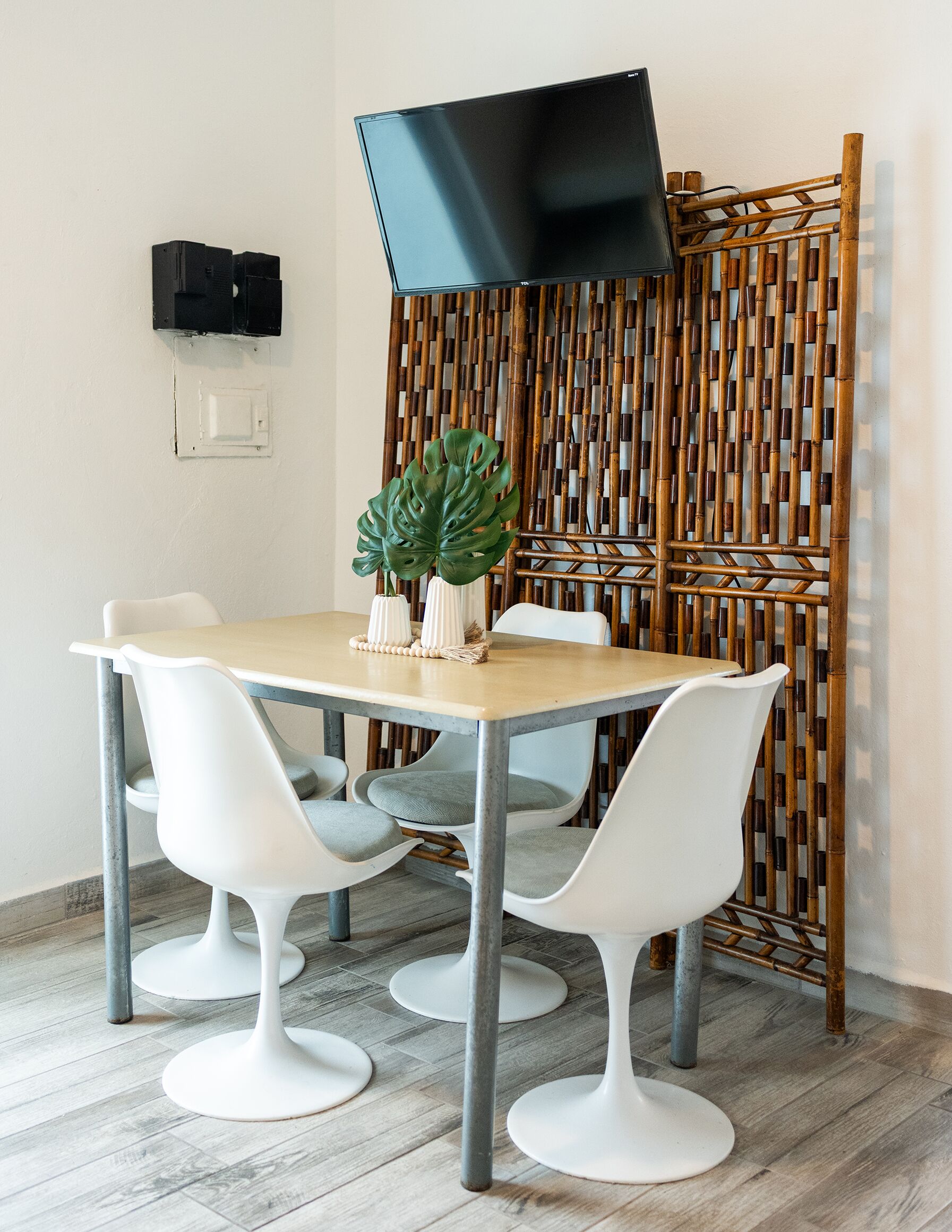 A dining area with a table, white chairs, a large plant, and a television mounted on the wall.