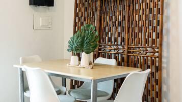A dining area with a table, white chairs, a large plant, and a television mounted on the wall.