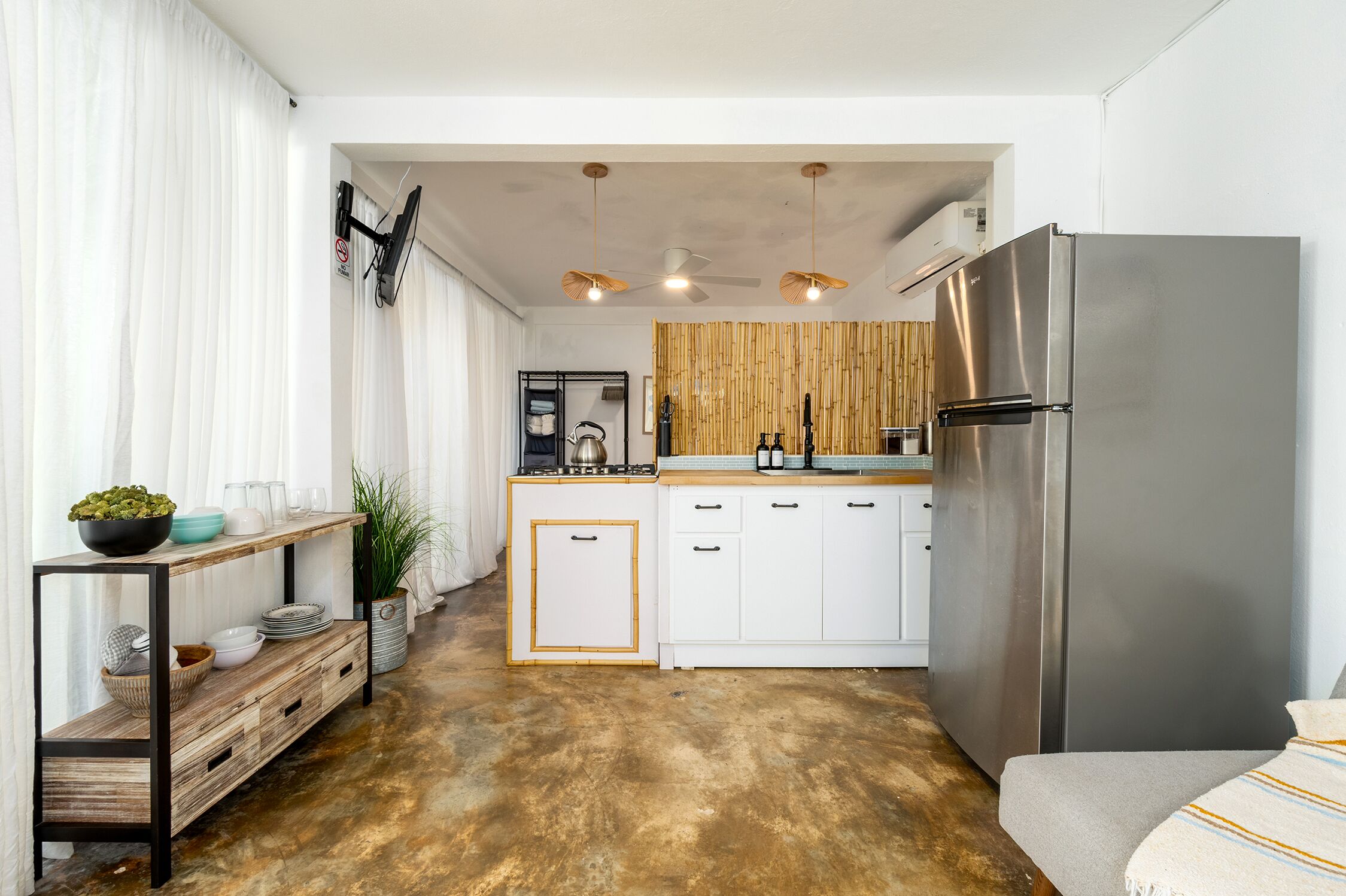 A compact kitchen with white cabinets, a stainless steel refrigerator, and a bamboo wall.