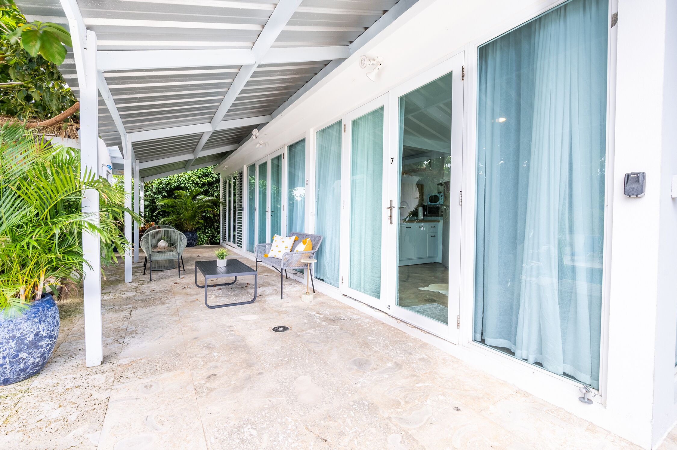 Un patio coperto con un angolo salotto, una pianta in vaso e vista sull'interno.