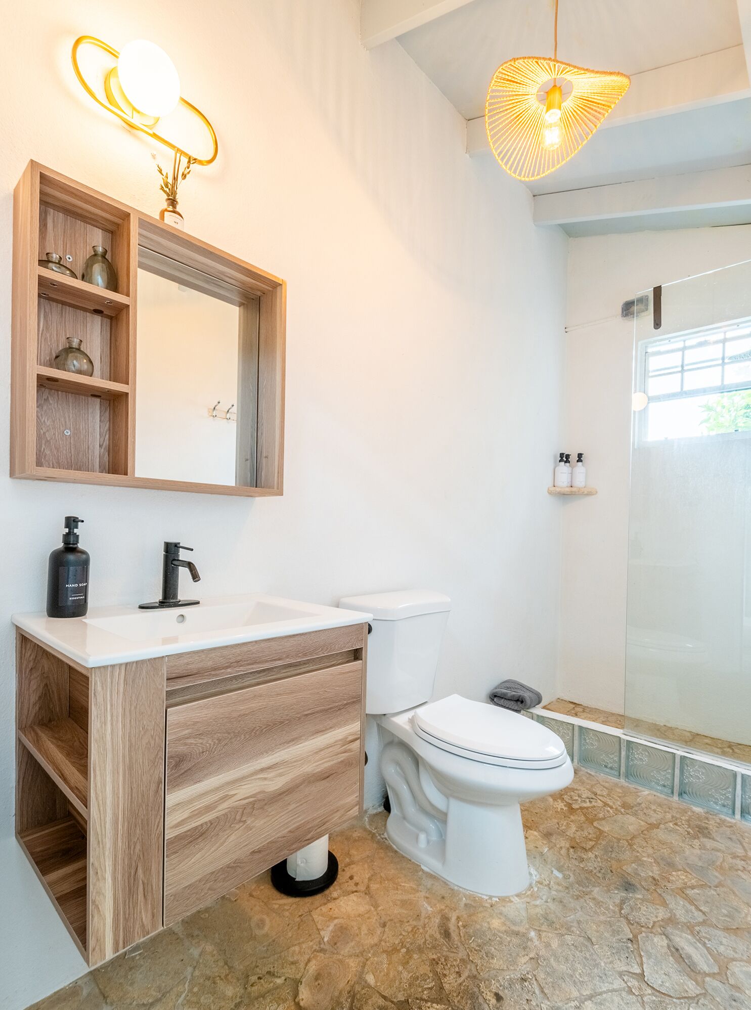 A bathroom with a wooden vanity, a white sink, a toilet, and a shower area.