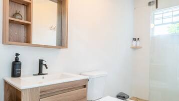 A bathroom with a wooden vanity, a white sink, a toilet, and a shower area.