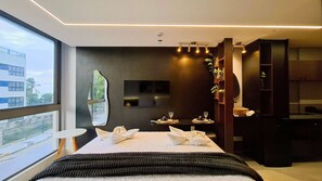Ein modernes Hotelzimmer mit einem großen Bett, einem Fernseher, einem kleinen Tisch mit einem Glas und Blick auf ein Gebäude.