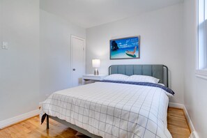 Ein Schlafzimmer mit einem Bett, einem Nachttisch, einem Wandbild und einem Fenster.