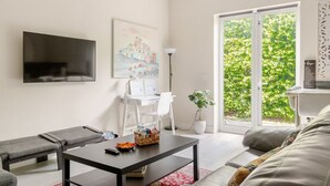 Una sala de estar moderna con un televisor de pantalla plana, un cuadro, un escritorio con una lámpara, una planta en maceta y un sofá.