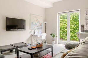 Una sala de estar moderna con un televisor de pantalla plana, un cuadro, un escritorio con una lámpara, una planta en maceta y un sofá.