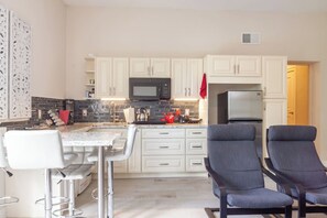 Una cocina moderna con armarios blancos, un microondas negro, un refrigerador de acero inoxidable y una barra con dos sillas.