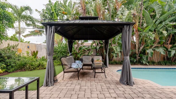 Un patio techado con piscina, mobiliario exterior y exuberante vegetación tropical.